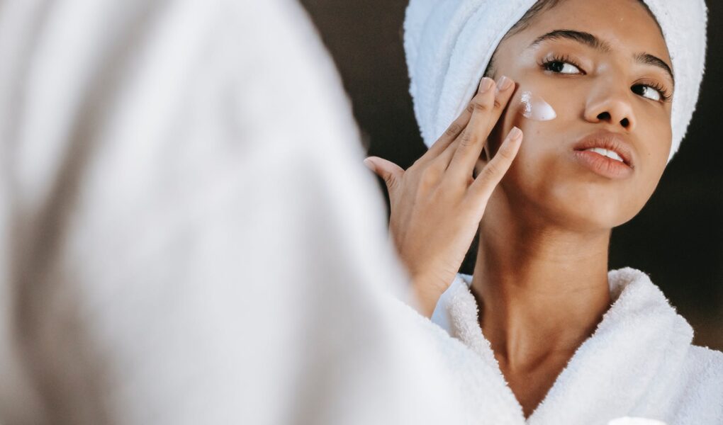 ethnic woman applying cream on face in morning