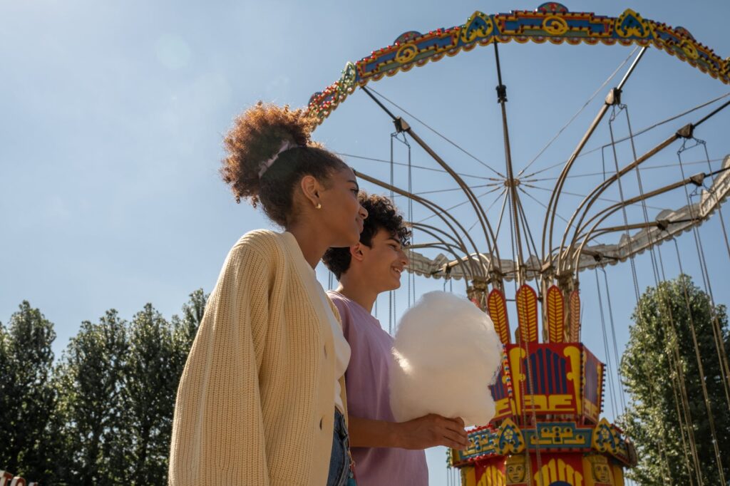 teenage couple walking by big carousel and boy holding cotton candy