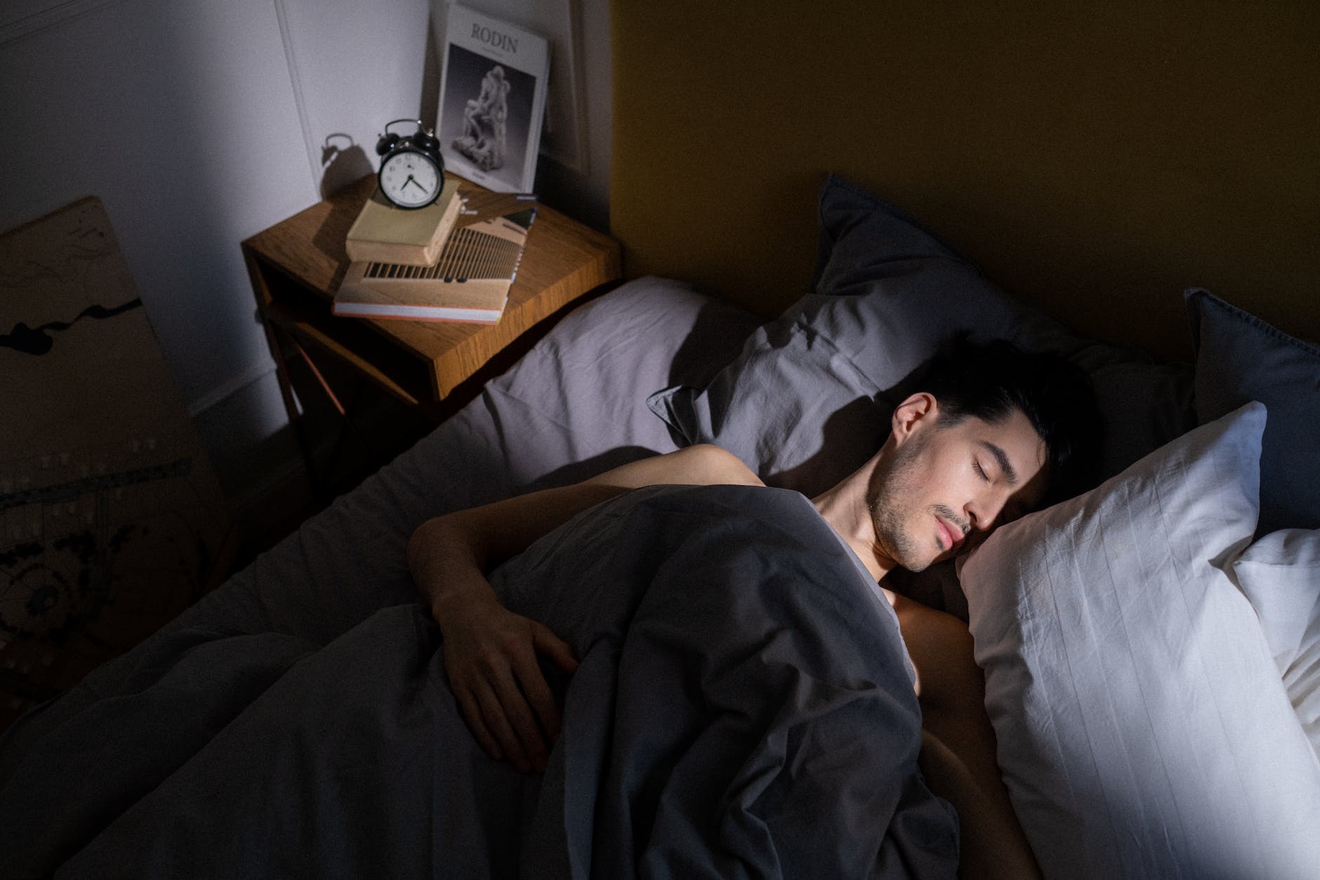 Man in bed still sleeping not harnessing discipline to get to bed to bed earlier to get more rest.
